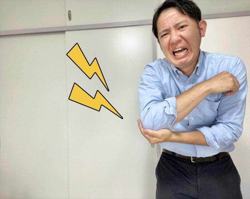 肘の鋭い痛みに顔をしかめる男性のイメージ—瞬間的に走る肘痛