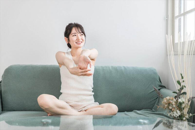 自宅ソファで前腕をやさしく伸ばす女性—家でできる腕のセルフケア例