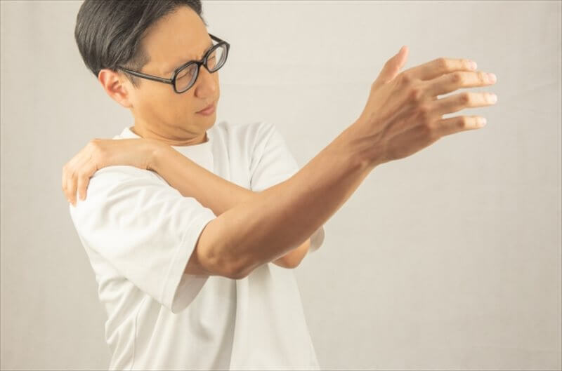 肩を押さえる男性のイメージ—首肩のこわばりが腕のしびれに関与する例