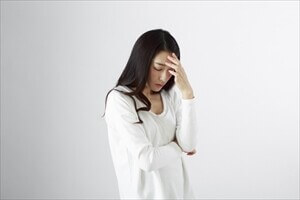片頭痛で頭を押さえる女性の写真