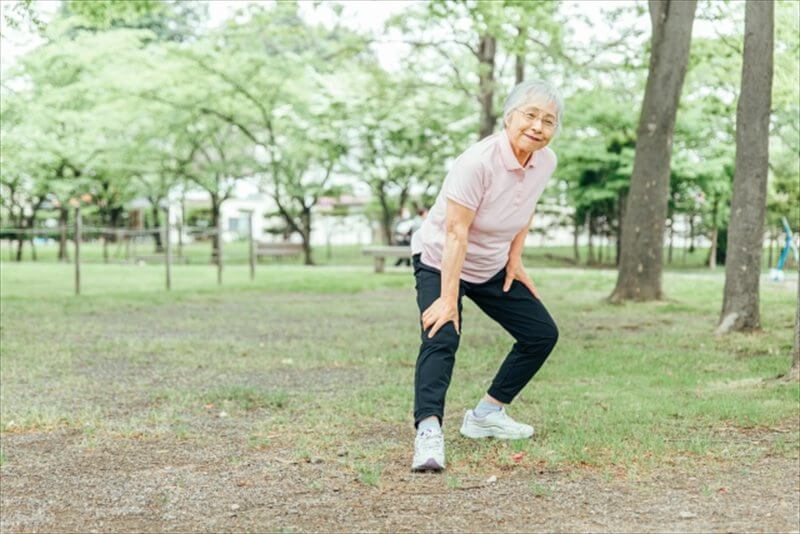 屋外で膝に手を当てて休む高齢女性 膝の重さを感じている様子