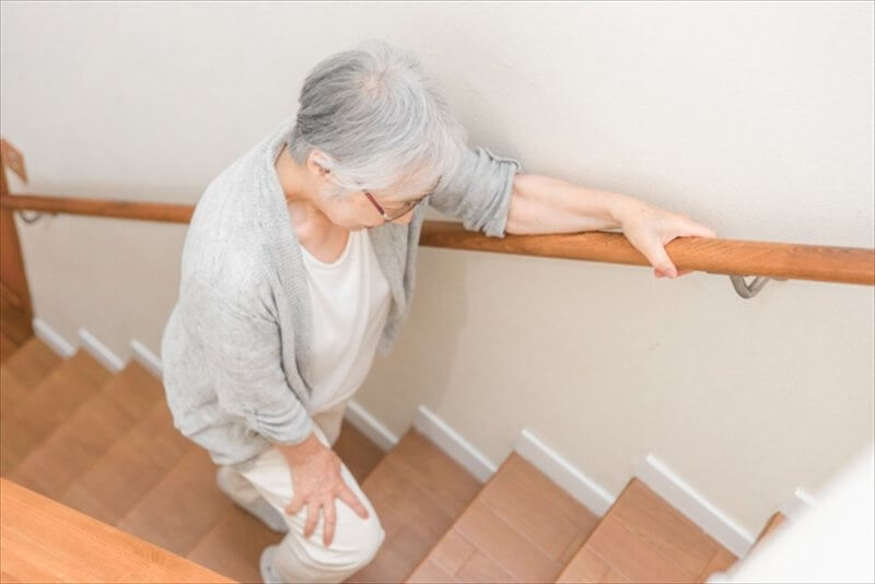 手すりを持ち一段ずつ階段を上がる女性 膝は第二趾の上を通す