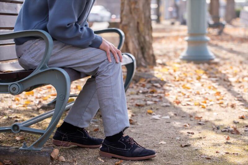 公園のベンチで膝に手を添えている男性 休みながら調整する様子