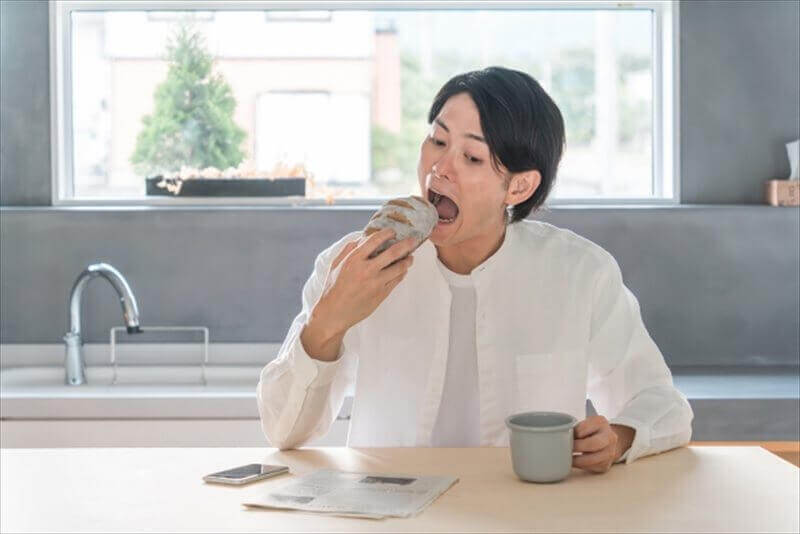 大口でパンを頬張る男性(顎に負担のかかる食べ方の例)