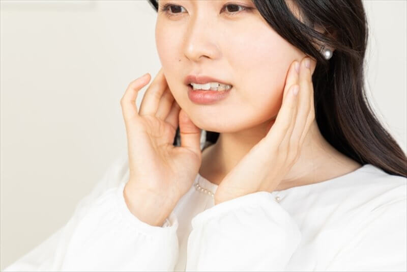あごの違和感を確かめる女性の横顔(両手で耳前を触れるセルフチェック)