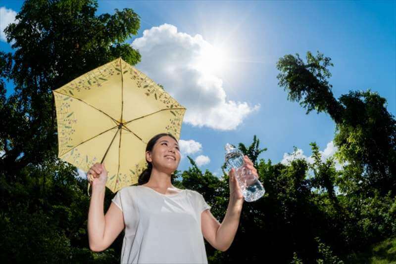 強い日差しの中、日傘と水を持つ女性