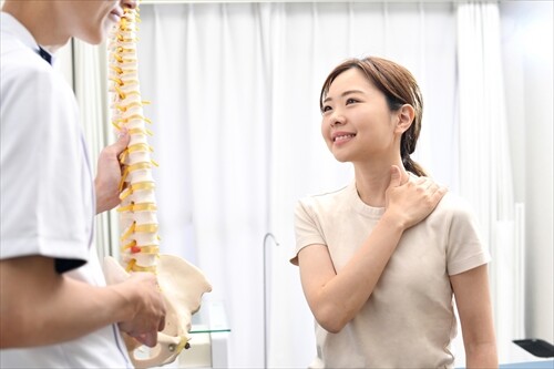 整骨院で説明を受ける女性と背骨模型を持つ施術者