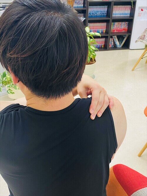 背中越しに肩を揉みほぐす男性の背面