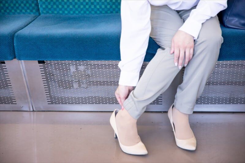 電車内で靴を触り足の違和感を確かめる女性