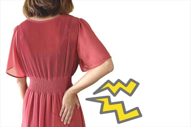 腰に痛みを感じて手を当てている女性の後ろ姿